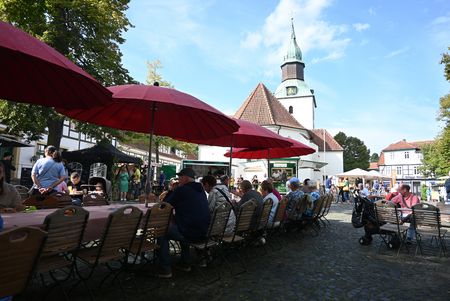 Besucher des Landmarktes Cittaslow in Bad Essen an langen Tischen mit Sonnenschirmen