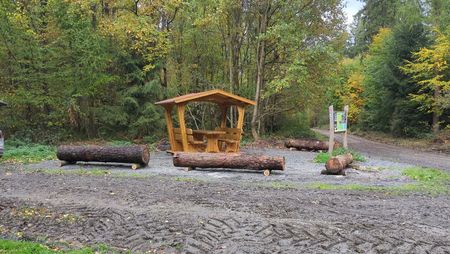 Rastplatz an einer Waldlichtung mit Hütte und Bänken sowie Hinweistafel